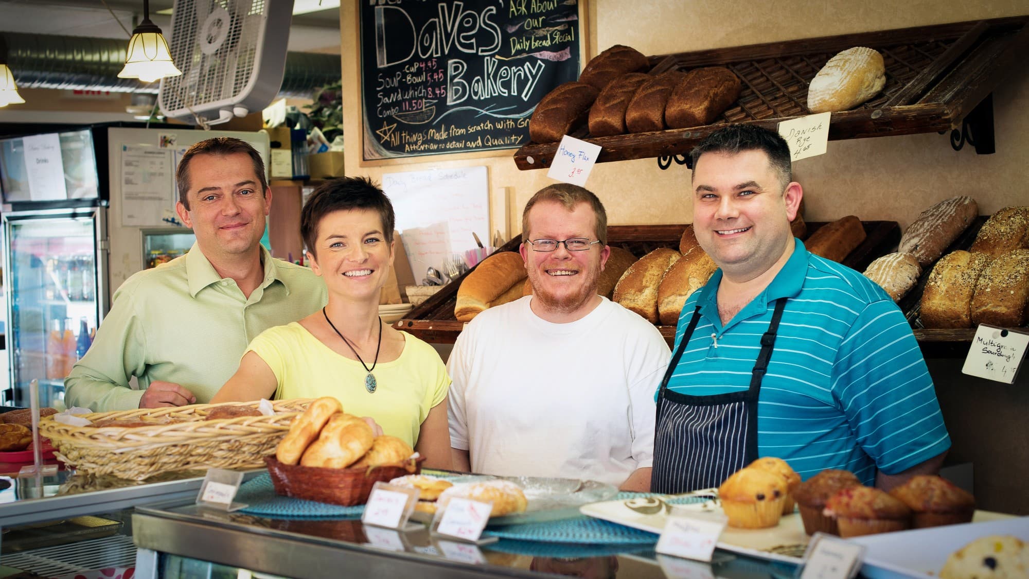 Behind the Daves' Bakery counter in 2014: the two Daves with visiting guests, bread racks full
